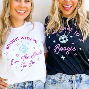 May include: Two women wearing matching t-shirts. One shirt is white with the text "BOOGIE WITH ME I'm The Bride To Be" in purple and light blue. The other shirt is black with the text "WELCOME TO Boogie" in pink and white.