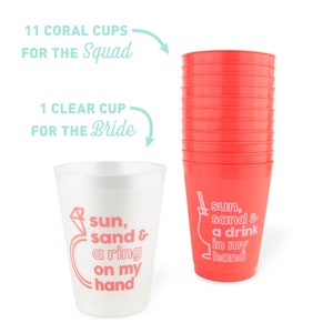 May include: A stack of eleven coral-colored plastic cups and one clear cup. The coral cups have a white graphic that says "sun, sand & a drink in my hand." The clear cup has a graphic that says "sun, sand & a ring on my hand."
