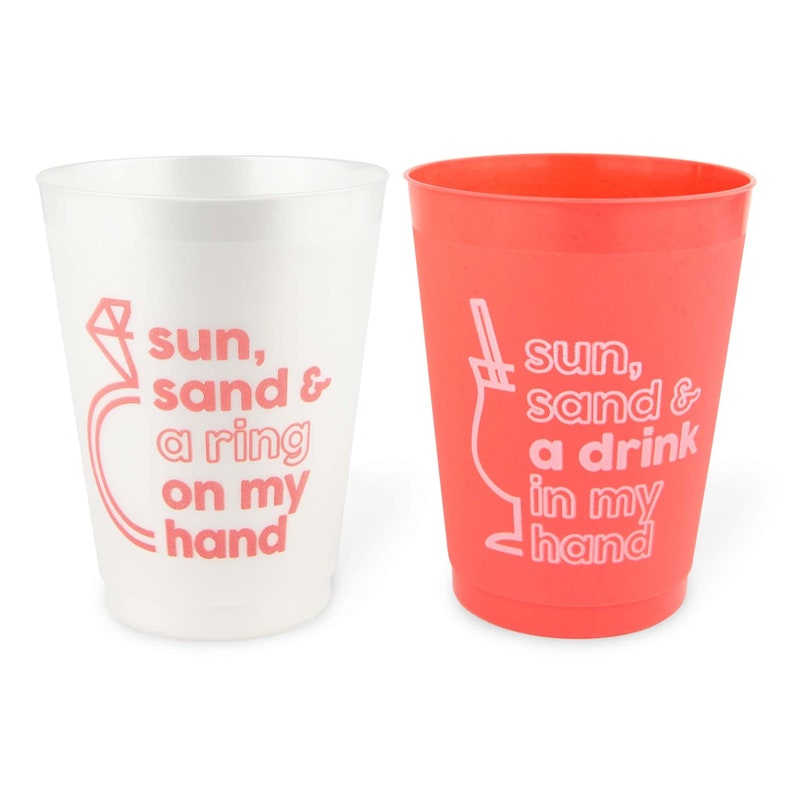 May include: Two plastic cups, one white and one coral. The white cup has a pink ring graphic and text that reads "sun, sand & a ring on my hand." The coral cup has a cocktail graphic and text that reads "sun, sand & a drink in my hand."
