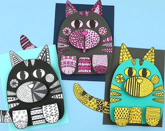 May include: Three paper cat crafts with different patterns and colors. The cats are black, gray, and turquoise with black outlines. The cats have different patterns on their bodies, including stripes, polka dots, and swirls.