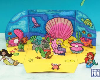 May include: A colorful pop-up card featuring mermaids, seashells, and other ocean creatures. The card is decorated with a blue and green ocean background and features the text "Super Fun Printables".