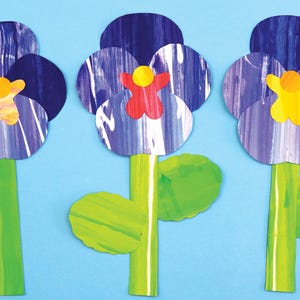 May include: Three paper pansies with blue petals, green leaves, and yellow and red centres. The pansies are on a light blue background.