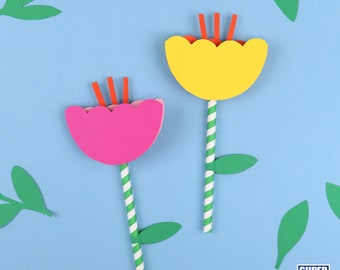 May include: Two paper flowers with green leaves and striped stems on a blue background. The flowers are yellow and pink with orange centers.