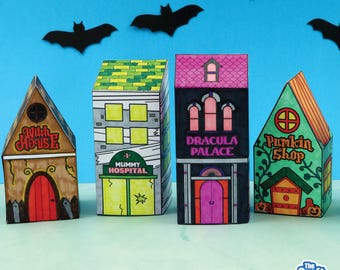 May include: Four colorful, handcrafted Halloween-themed paper houses. The houses are labeled "Witch House", "Mummy Hospital", "Dracula Palace", and "Pumpkin Shop". Black bat cutouts are arranged against a blue background.