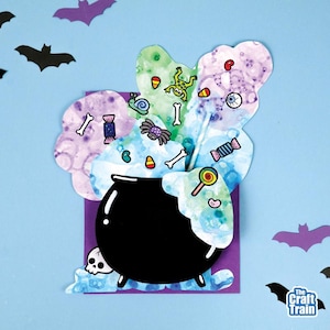 May include: A black cauldron craft project featuring colorful bubble-painted cutouts of green, blue, and purple smoke. The scene includes small illustrations of a frog, snail, spider, skull, bones, and candy, with paper bats scattered around.