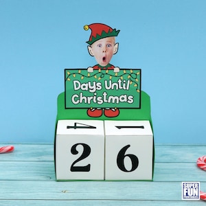 May include: A printable Christmas countdown calendar featuring a green elf with a red hat holding a sign that says "Days Until Christmas". The calendar has two white cubes with the numbers 26 and 4 printed on them.