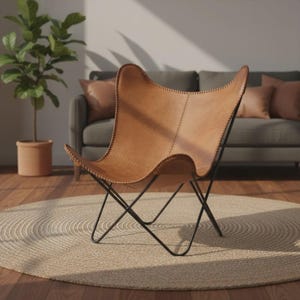 May include: A tan leather butterfly chair with a black metal frame. The chair has a distinctive butterfly wing shape and is stitched along the edges. The chair is placed on a round jute rug.