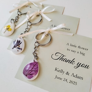 Personalisierte Gastgeschenke für die Hochzeit. Gastgeschenk zur Brautparty, Babyparty. Schlüsselanhänger mit gepressten Blumen auf weißem Hintergrund.