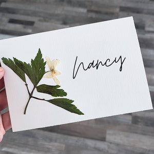 Handgemaakte geperste bloemenplaatskaarten met ECHTE bloemen en gepersonaliseerde, gedrukte tekst aan de binnenkant. Gepersonaliseerde naamkaartjes met weidebloemen.