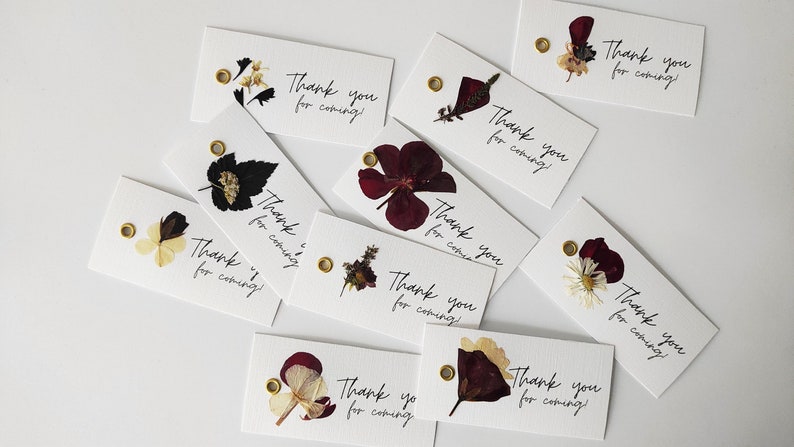 May include: A collection of white thank you tags with pressed flowers and gold eyelets. The tags have the text "Thank you for coming!" written in black calligraphy.