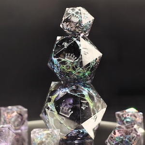 May include: A stack of three iridescent, multi-faceted dice with crown symbols. The dice are clear with a mix of colors, including green, blue, and purple. Several smaller dice are scattered around the base of the stack.