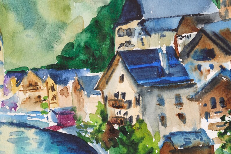 Puede incluir: Pintura a la acuarela de un pueblo europeo enclavado contra una monta&ntilde;a verde. Los edificios tienen paredes marrones y beige con tejados azules. La escena incluye un r&iacute;o en primer plano, con follaje verde y morado.