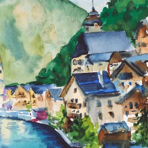 Puede incluir: Pintura a la acuarela de un pueblo junto al lago, enclavado contra una monta&ntilde;a verde. Los edificios con tejados azules y paredes beige bordean la orilla del agua. El agua es una mezcla de azul y turquesa, y el cielo es azul claro.