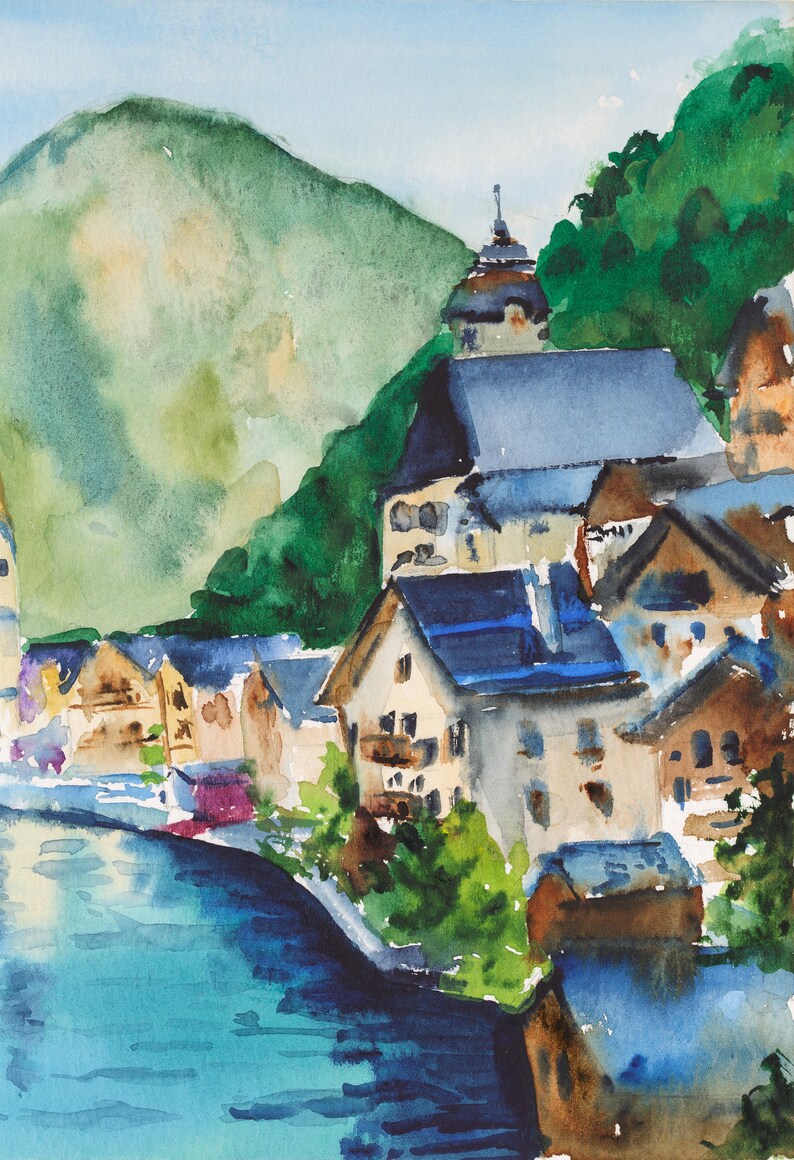 Puede incluir: Pintura a la acuarela de un pueblo junto al lago, enclavado contra una monta&ntilde;a verde. Los edificios con tejados azules y paredes beige bordean la orilla del agua. El agua es una mezcla de azul y turquesa, y el cielo es azul claro.