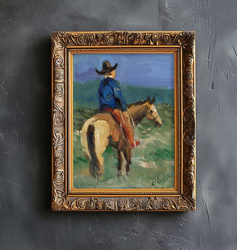 May include: An oil painting in a decorative gold frame depicting a person wearing a cowboy hat and blue jacket riding a tan horse through a green field. The scene features a blue sky and a signature in the bottom right corner of the canvas.