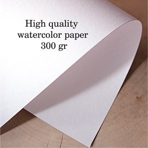 Puede incluir: Primer plano de una pila de papel de acuarela blanco. El texto en el papel dice "High quality watercolor paper 300 gr". El papel est&aacute; ligeramente curvado, revelando su grosor y textura.