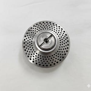 Może przedstawiać: Okrągły metalowy element z licznymi małymi otworami rozmieszczonymi wokół centralnej piasty. Piasta posiada łeb śruby z nacięciem. Element ma matowe, metaliczne wykończenie i wydaje się być wykonany ze stali.