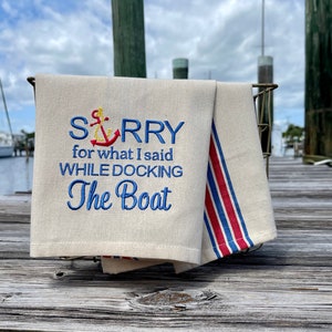 May include: A white kitchen towel with blue and red stripes. The towel has an embroidered anchor and the text "SORRY for what I said WHILE DOCKING The Boat".