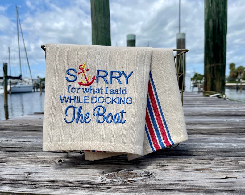 May include: A white kitchen towel with blue and red stripes. The towel has an embroidered anchor and the text "SORRY for what I said WHILE DOCKING The Boat".