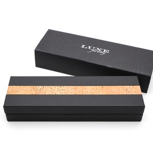 May include: Two rectangular boxes for writing instruments. One box is solid black with the white text LUXE fine writing. The other box features a textured black finish with a horizontal strip of natural tan cork running across the center.