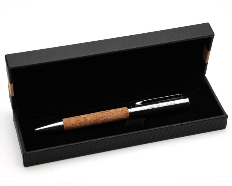 May include: A ballpoint pen with a natural cork grip and a polished silver-tone metal cap and tip. The cap features the engraved name Sophia Scott. The pen is presented inside a rectangular black gift box with a textured exterior and black lining.