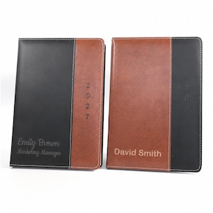 Op de afbeelding: Twee rechthoekige planners met een tweekleurig ontwerp en verticale stiksels. De linker planner is zwart met een bruin zijpaneel, gepersonaliseerd met 'Emily Brown Marketing Manager' en '2027'. De rechter is bruin met een zwart paneel, 'David Smith' en '2027'.