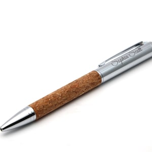 May include: A ballpoint pen featuring a natural brown cork barrel and polished silver-tone metal accents. The cap includes a pocket clip and the engraved name Sophia Scott in a cursive script font. The tip and end cap are also silver-tone metal.