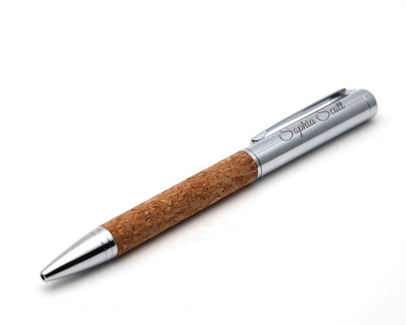 May include: A ballpoint pen featuring a natural brown cork barrel and polished silver-tone metal accents. The cap includes a pocket clip and the engraved name Sophia Scott in a cursive script font. The tip and end cap are also silver-tone metal.