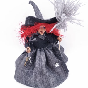 May include: A handmade witch doll with red hair, a black hat, and a gray dress. She is holding a broom and a set of keys.