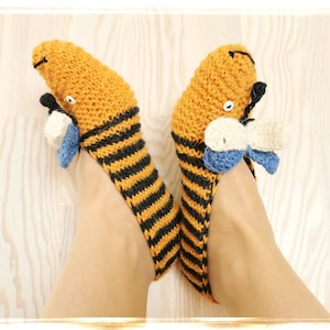Puede incluir: Un par de zapatillas de punto de rayas amarillas y negras con un diseño de mariposa en los dedos. Las mariposas están hechas de hilo blanco, azul y amarillo.