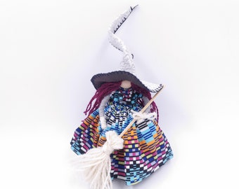 May include: A handmade witch doll with a long white pointed hat, burgundy hair, and a colorful patterned dress. She is holding a white yarn broom.