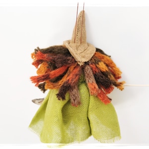 May include: A handmade witch doll with a brown burlap hat, a green burlap skirt, and a long, colorful yarn hair.