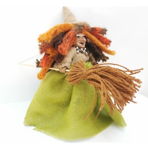 May include: A handmade witch doll with a brown burlap dress, a green burlap skirt, and a brown broom. The doll has a brown hat, orange and brown hair, and a painted face.