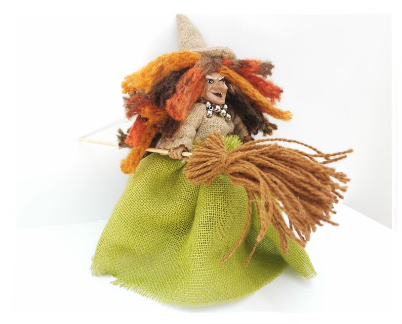 May include: A handmade witch doll with a brown burlap dress, a green burlap skirt, and a brown broom. The doll has a brown hat, orange and brown hair, and a painted face.