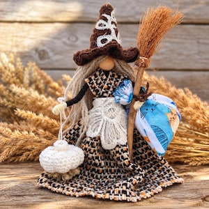 Peut inclure: Une poupée artisanale portant un chapeau de sorcière en crochet marron avec des broderies blanches, une robe tissée texturée marron et orange, et un tablier en dentelle blanche. Elle a des cheveux en laine, un balai, une citrouille en crochet.