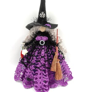 May include: A purple and black crocheted witch doll with a black pointed hat, a broom, and a red and white flower.