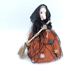Può includere: Bambola di strega fatta a mano con un velo nero e un vestito arancione. La bambola tiene in mano una scopa e un portachiavi a forma di chiave. L'abito è decorato con una rete nera e piccoli abbellimenti floreali. Decorazione di Halloween.