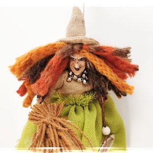 May include: A witch doll with long, orange, brown, and red yarn hair, wearing a brown burlap dress and hat, holding a brown yarn broom.