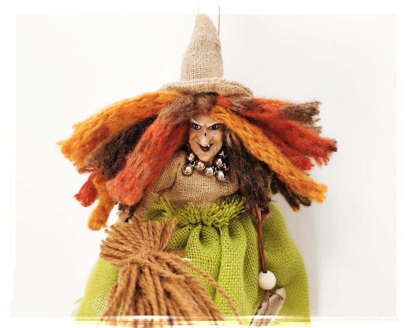 May include: A witch doll with long, orange, brown, and red yarn hair, wearing a brown burlap dress and hat, holding a brown yarn broom.
