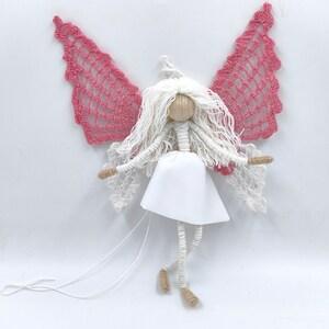 May include: A handmade white yarn angel doll with pink crocheted wings and a white fabric dress. The doll has a wooden head and is strung with white yarn for arms and legs.