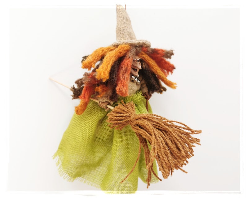 May include: A handmade witch doll with a brown, orange, and yellow yarn wig, a green burlap skirt, and a brown yarn broom.