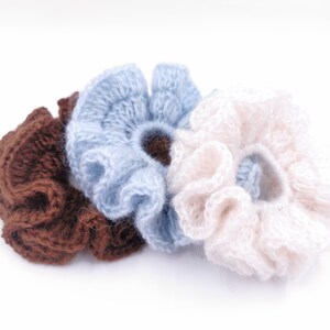 Puede incluir: Tres scrunchies de pelo de ganchillo en marrón, azul claro y crema.