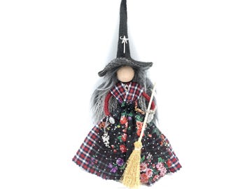 Può includere: Una bambola strega stravagante con un cappello nero alto adornato da una stella bianca. La bambola ha i capelli grigi, un top a quadri e una gonna con stampa floreale. Tiene una scopa e una collana con ciondoli, perfetta per Halloween.