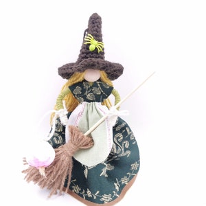 May include: A handmade witch doll with brown yarn hair, a brown crocheted hat with a green spider, a green and gold dress, and a brown broom.
