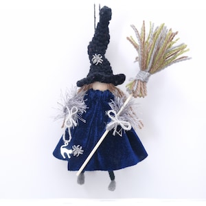 May include: A handmade witch doll ornament with a black crocheted hat, a blue velvet dress, and a broom made of yarn. The doll has a silver charm of a cat and a spider on its dress.