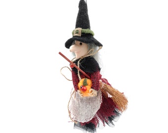 Può includere: Bambola di strega di Halloween con cappello nero, vestito rosso e nero e scopa. La strega ha i capelli grigi e tiene in mano una zucca con una coccinella. La bambola è fatta di tessuto e ha un aspetto rustico.