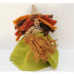 May include: A handmade witch doll with a green skirt, brown yarn hair, and a brown yarn broom. The doll has a painted face with a mischievous expression and wears a brown hat.