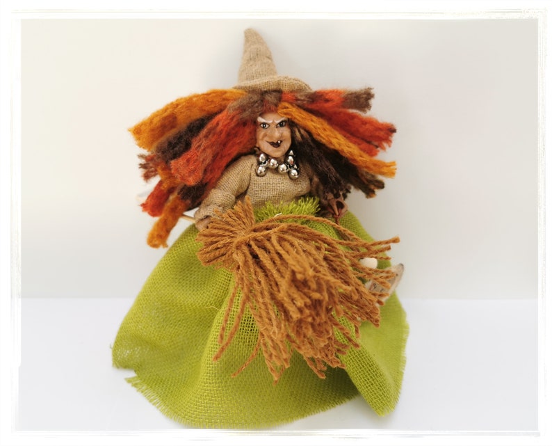 May include: A handmade witch doll with a green skirt, brown yarn hair, and a brown yarn broom. The doll has a painted face with a mischievous expression and wears a brown hat.