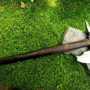 May include: A black-handled axe with a silver blade and a curved edge. The axe is lying on a green mossy surface.