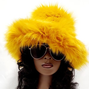 May include: A bright yellow faux fur bucket hat with a fluffy pom pom on top. The hat is worn by a person with dark hair and sunglasses.
